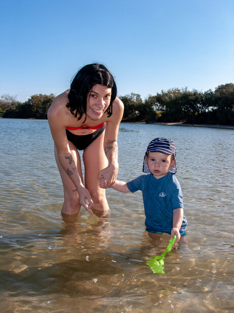 Woman and toddler wading in shallow water at a beach on a clear day.