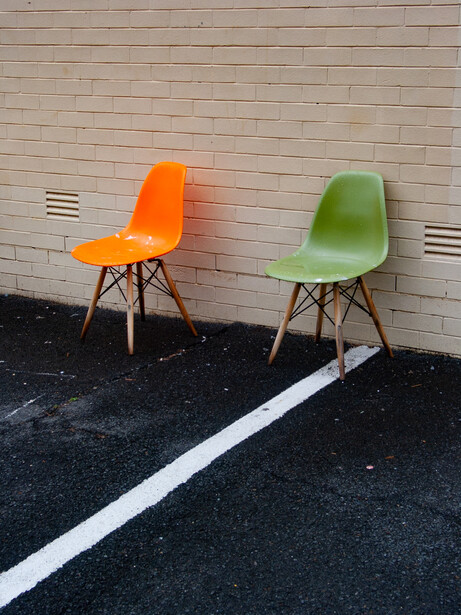 Orange and green mid-century modern chairs facing each other across a white line on dark pavement.