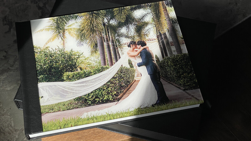Wedding photo album displayed open, showing bride and groom kissing beneath palm trees with flowing veil.