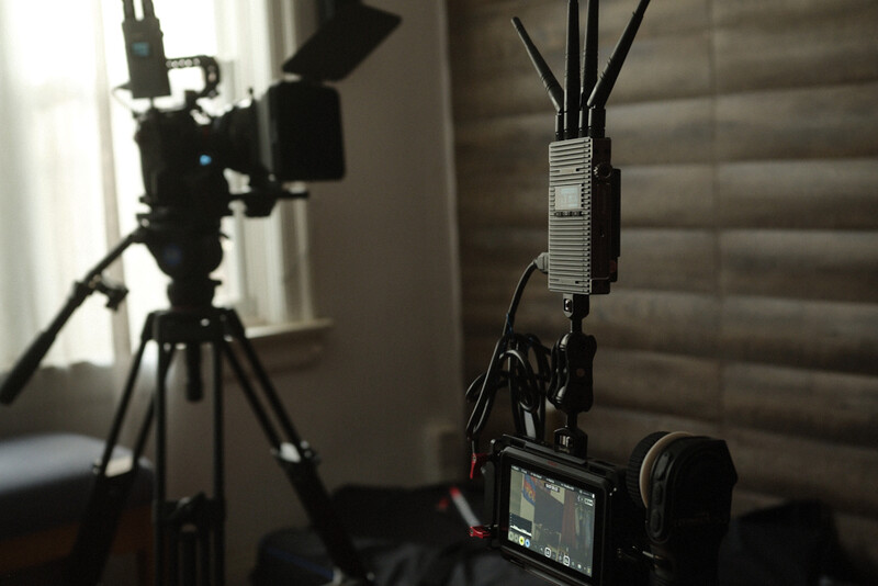 Professional video production setup with camera on tripod, wireless microphone receiver, and key light in studio environment.