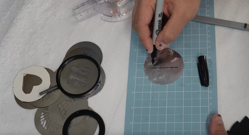 Hands cutting circular lens filter samples on a self-healing cutting mat using a ruler and utility knife.