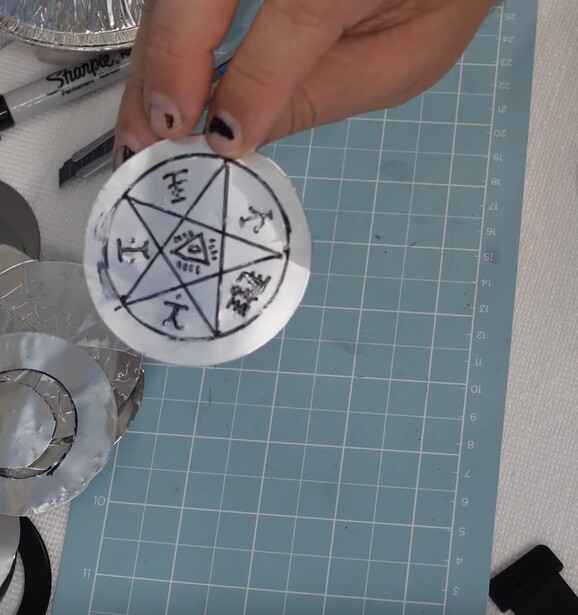 Hands holding a circular diagram with astrological symbols and divisions on a gridded cutting mat.