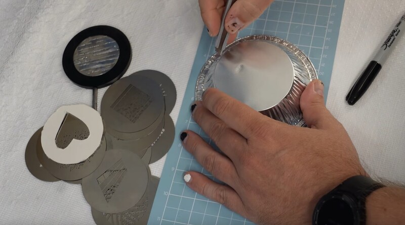 Hands cutting circular stencil templates from tan paper on a blue cutting mat with craft tools nearby.