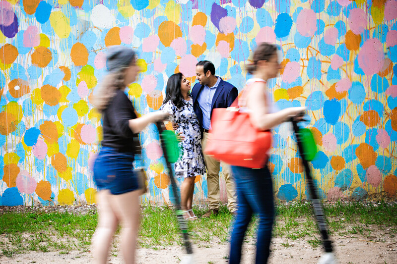 Two people in motion blur stand against a vibrant polka-dot mural while a couple poses in the center.