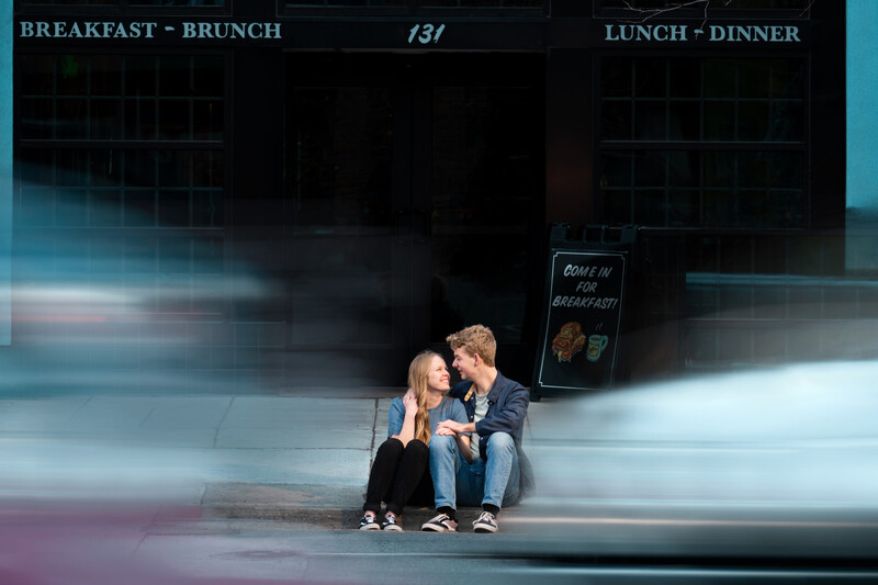 Two people sitting against a storefront with motion blur creating streaking light effects around them.