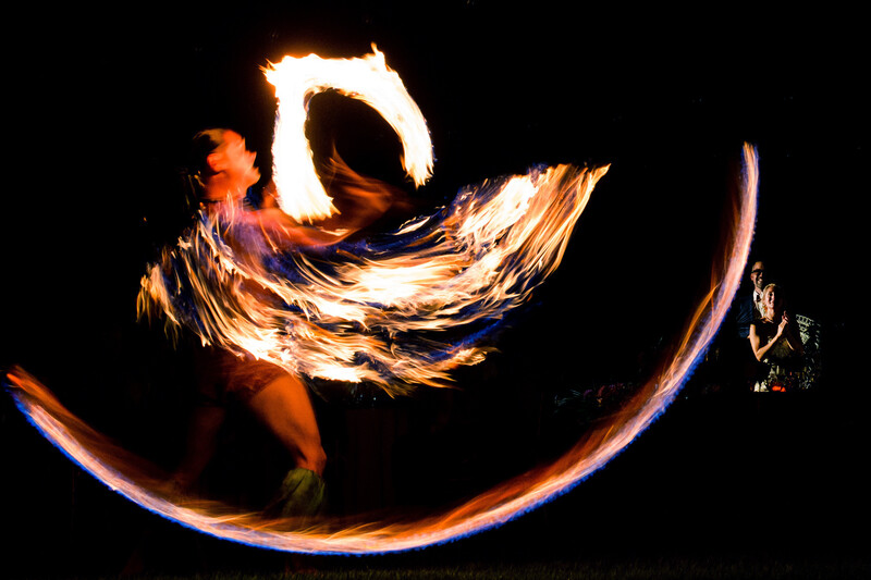 Fire spinner performing with long exposure light trails creating glowing arcs and swirls against black night sky.