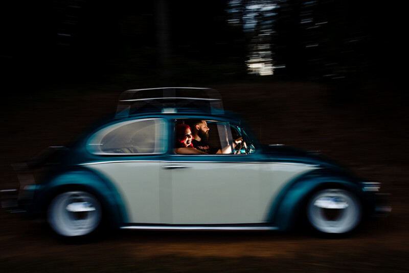 Blue and white vintage Beetle captured in motion blur with occupants visible through illuminated windows at night.