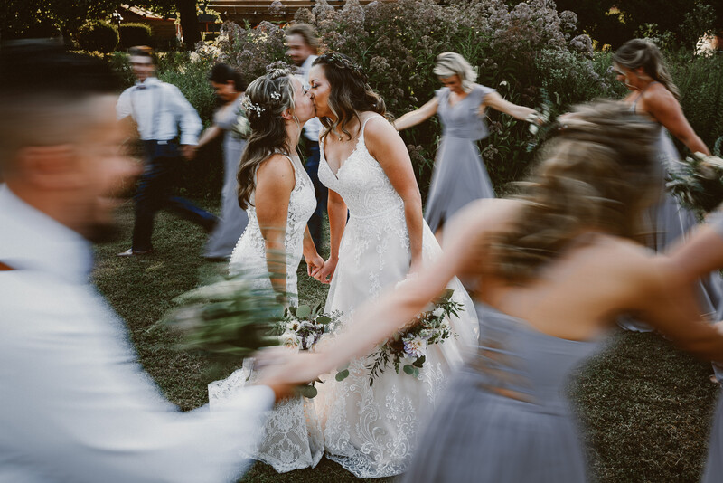 Bride in white lace dress dancing with guests in motion blur at outdoor wedding reception.