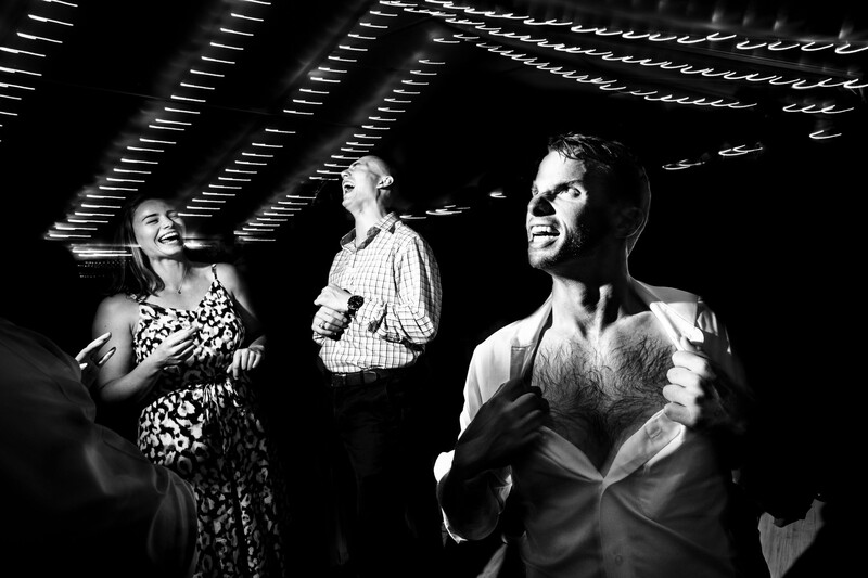 Three people laughing together indoors under geometric ceiling lights in black and white.