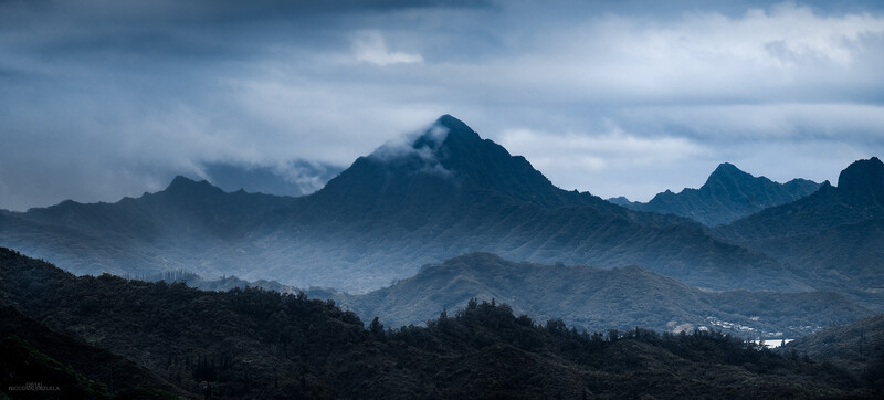 Layered mountain ridges receding into atmospheric haze under a moody blue sky.