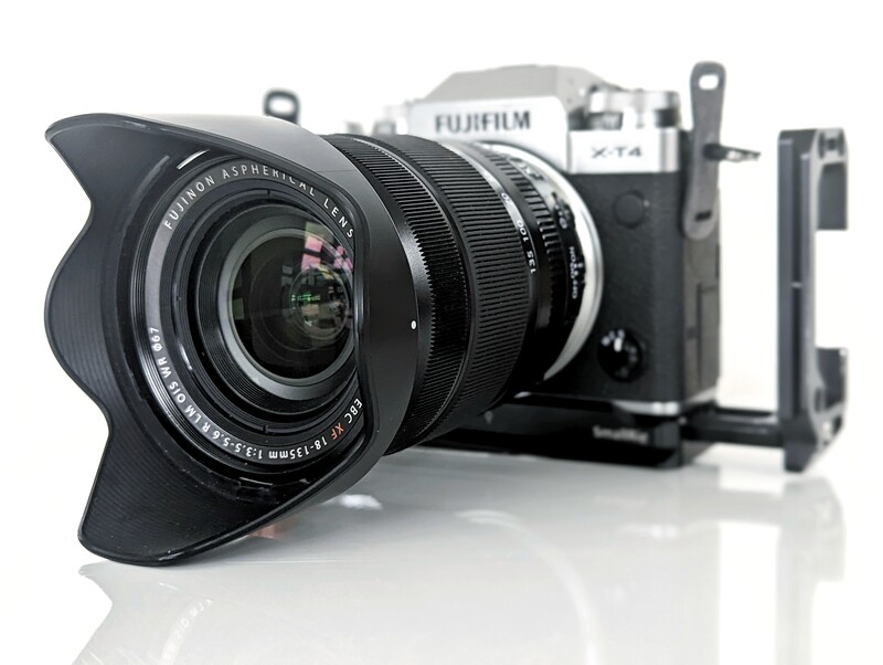 Fujifilm camera with wide-angle lens and lens hood attached, displayed with accessories including a lens cap holder and mounting plate.