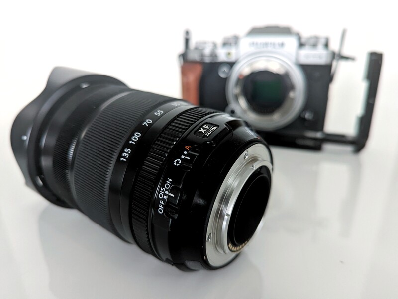 Vintage rangefinder lens in foreground with film camera body blurred in background.