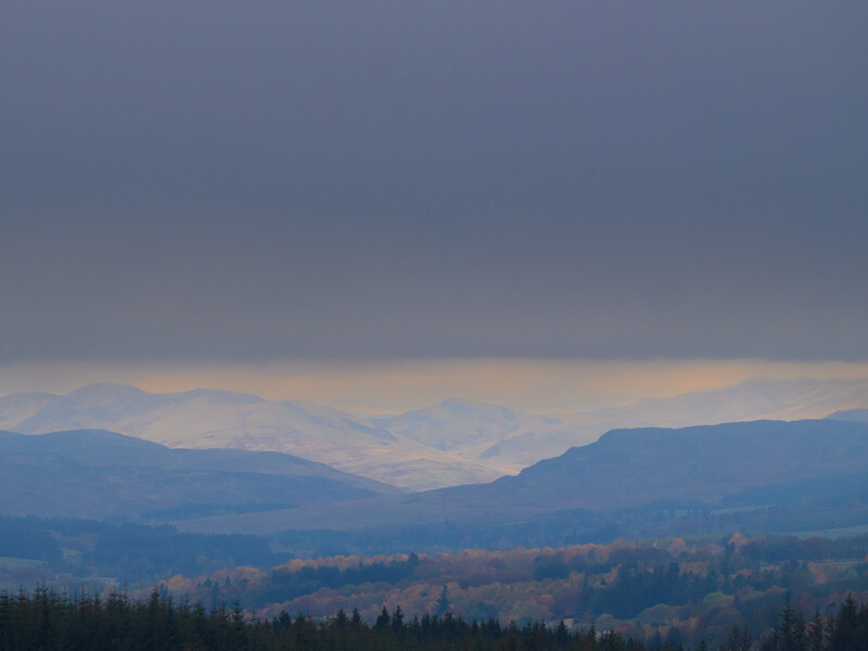 Layered mountain ranges receding into hazy distance under overcast sky with forested foreground.