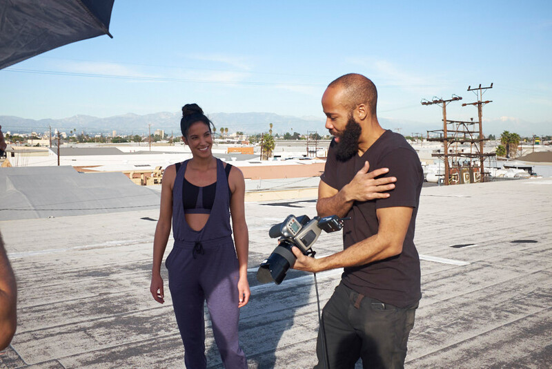 Videographer holding a cinema camera while reviewing footage with a female subject on a rooftop.