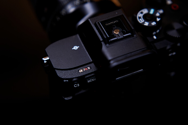 Sony Alpha camera body with LCD screen visible, displayed alongside a camera flash unit on dark surface.