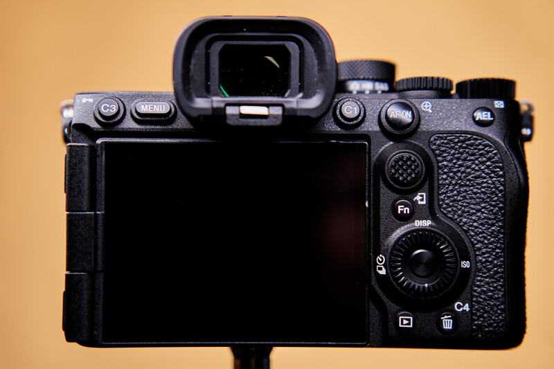 Rear view of a mirrorless camera body with articulating screen displayed against tan background.