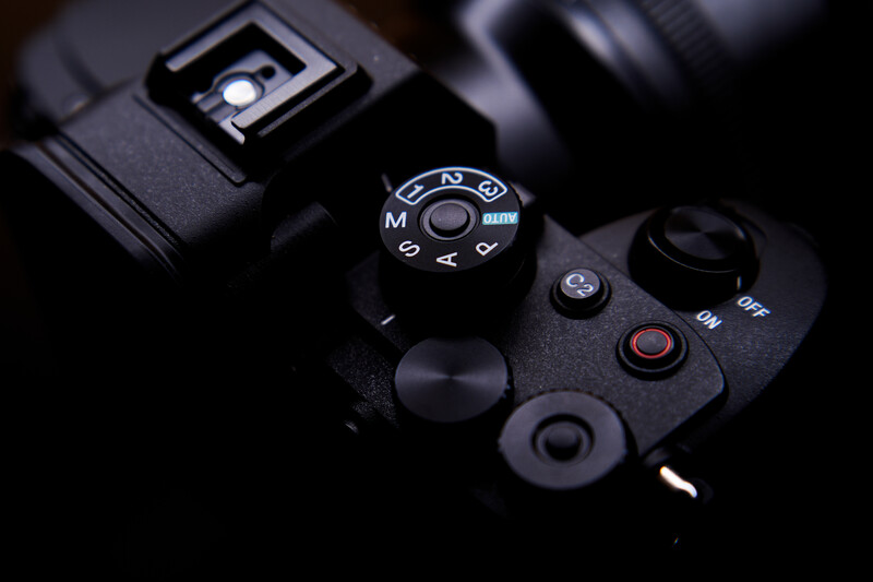 Close-up of a camera's mode dial and control buttons with dramatic side lighting against a dark background.