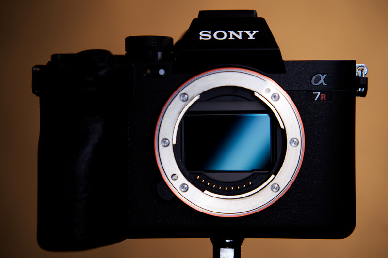 Sony α7 II mirrorless camera body with open sensor and mirror, shown against warm tan background.