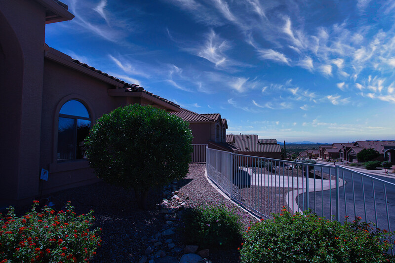 Residential rooftop terrace with metal railing overlooking suburban landscape under blue sky.