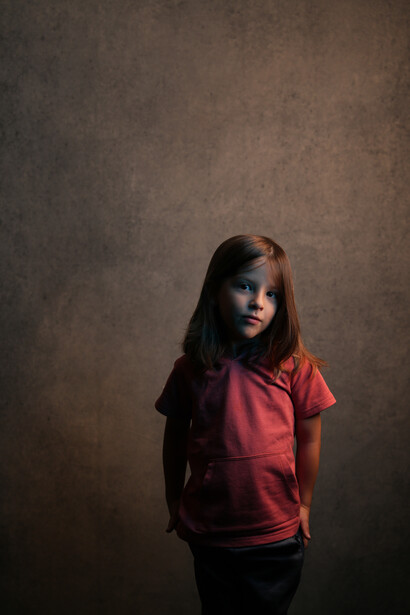 Young girl in red t-shirt against textured brown studio backdrop.