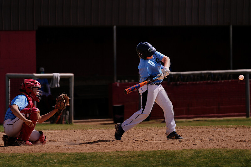 Baseball batter mid-swing during an evening game under stadium lights while catcher crouches behind home plate.