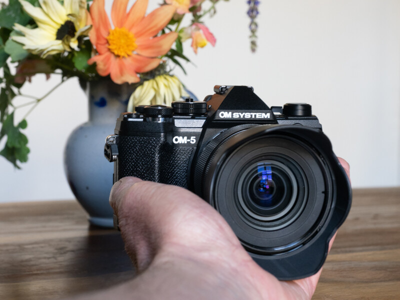 OM-G film camera held in hand with colorful flowers in vase in background.