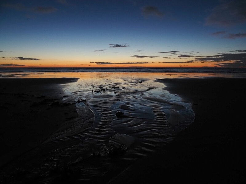 Tidal flats with rippled water patterns reflecting an orange and blue sunset sky.