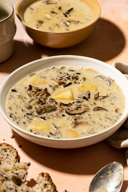 Two bowls of creamy soup garnished with seeds and potato slices on a warm-toned surface.