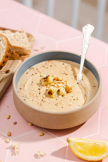 Bowl of creamy hummus garnished with olive oil and spices, served with toasted bread slices and lemon wedge.