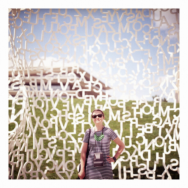 Person standing in front of large white text wall installation against sky backdrop.