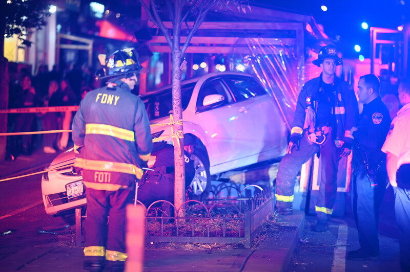 FDNY firefighters respond to a vehicle that has struck a tree at night, illuminated by emergency lighting.