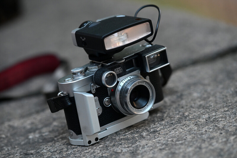 Vintage rangefinder camera with built-in flash and viewfinder mounted on concrete surface.