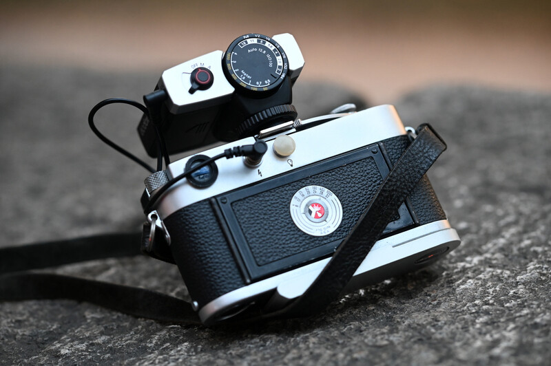 Two vintage rangefinder cameras with black leather bodies and chrome trim stacked on concrete.
