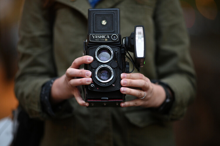 Hands holding a Yashica twin-lens reflex camera with a light meter attachment.