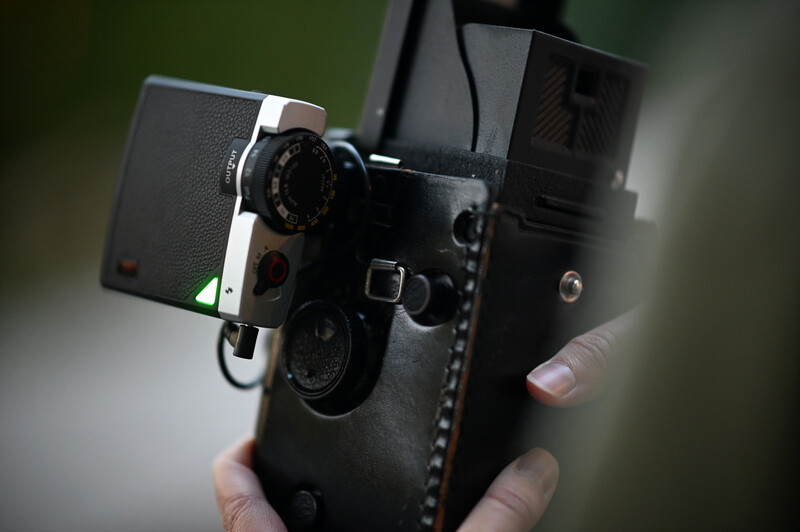 Vintage 16mm film camera with leather carrying case held in someone's hands.