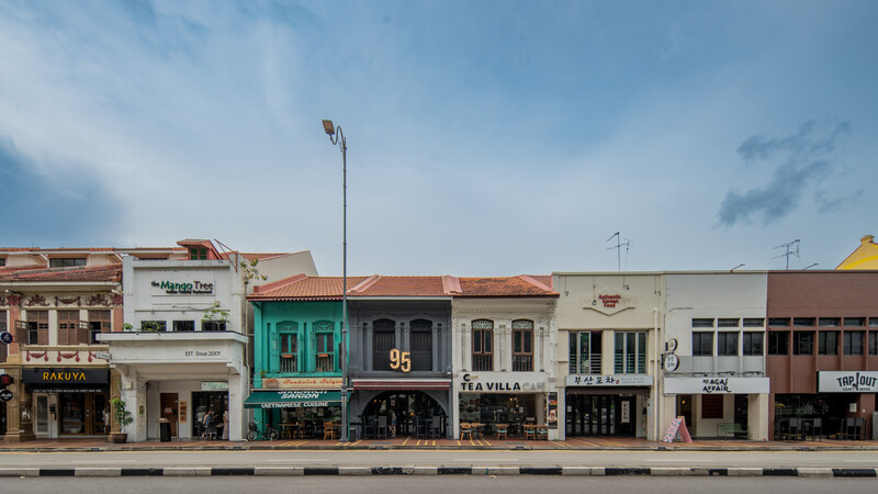 Row of colorful vintage storefronts with varied architectural styles and weathered facades along a street.