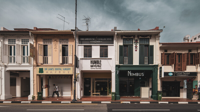 Row of colorful shophouse facades with varied architectural styles under dramatic cloudy sky.
