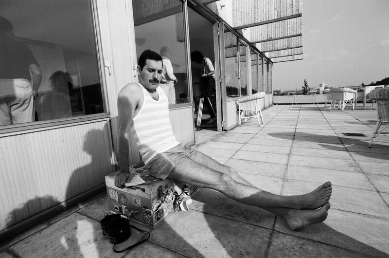 Man in white tank top sitting on rooftop with legs extended, shot in black and white.
