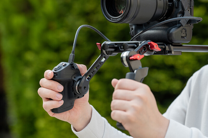 Cinematographer holding a camera rig with follow focus wheel and red handles mounted on rails.