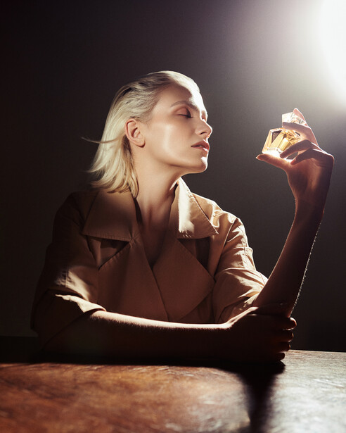 Woman in profile holding a glass, backlit by warm spotlight against dark background.