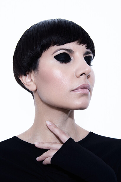 Profile portrait of a person with dark blunt bangs and pale complexion against a white background.