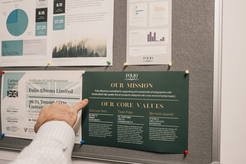 Person pointing to a green portfolio presentation board displaying mission and core values during a design review.