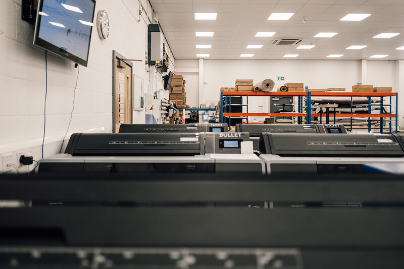 Large-format printer in a bright, well-lit workspace with shelving and storage in the background.