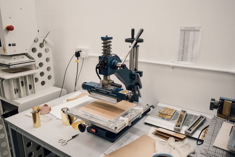 Blue printing press with wooden substrate positioned on work table in studio setting.