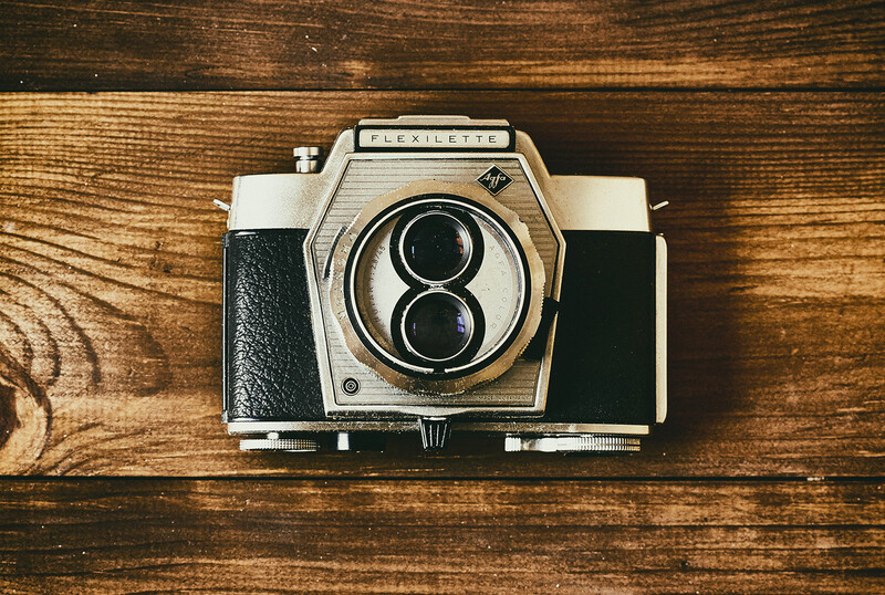Vintage twin-lens reflex camera with white and black body on wooden surface.