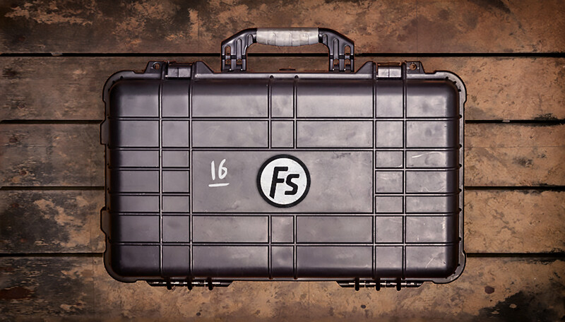 Black protective equipment case with white logo and number 16 marked on the lid, photographed overhead on a weathered wooden surface.
