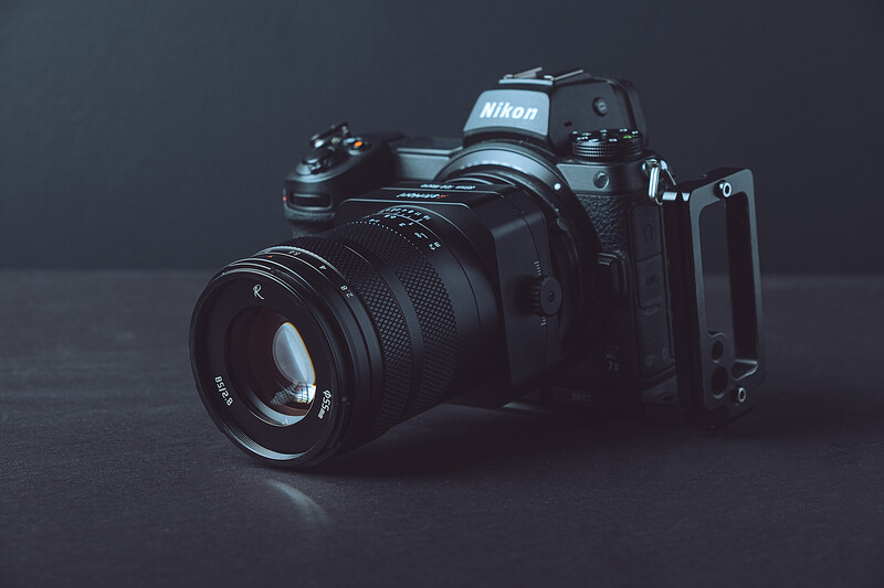 Nikon film SLR camera with standard prime lens on dark surface against gray backdrop.