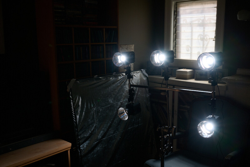 Professional studio lighting setup with four bright LED panel lights positioned around a black diffusion panel in a darkened room.