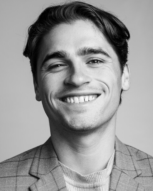 Black and white portrait of a smiling man with dark hair wearing a button-up shirt and blazer.