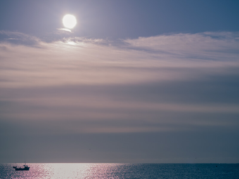 Full moon rising over calm ocean waters with soft pink and blue sky at twilight.